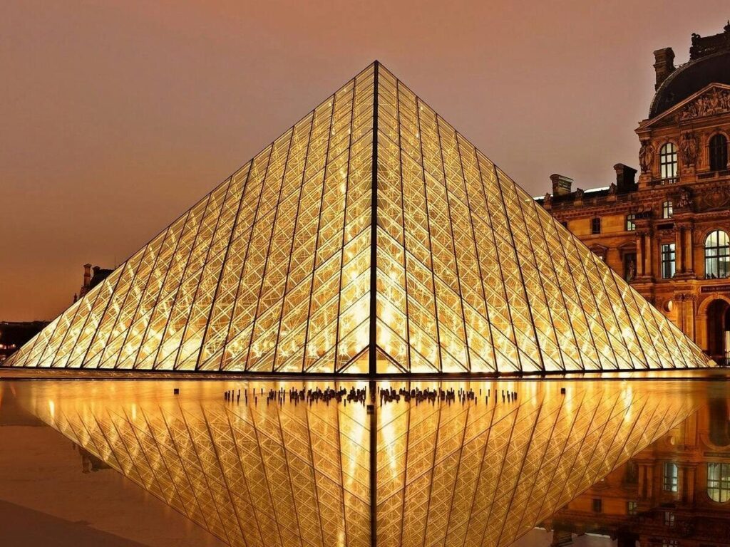 Stunning nighttime view of the illuminated Louvre Pyramid and reflection in Paris, France.
